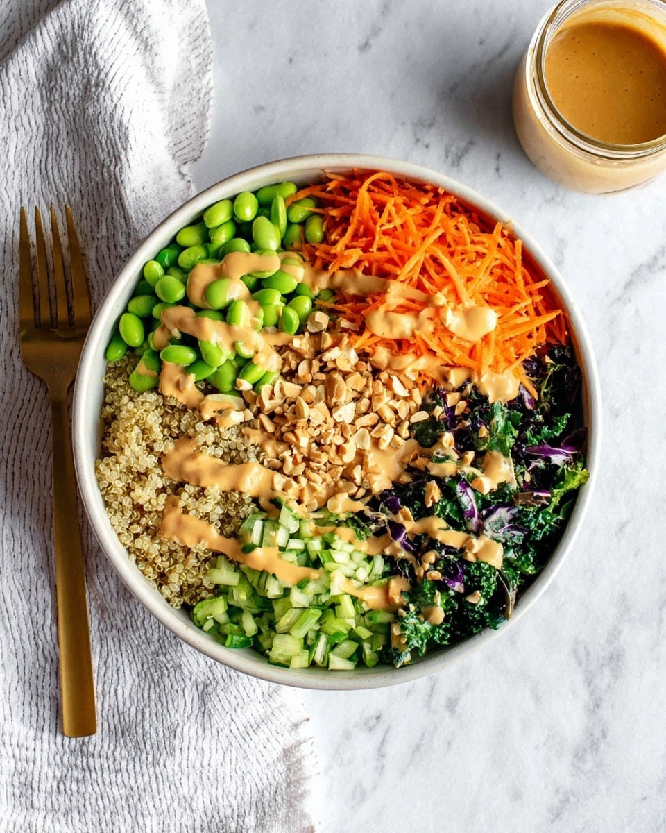 A white bowl filled with five colorful layers arranged in sections: bright green edamame in the top center, shredded orange carrots on the top right, dark green kale on the bottom right, chopped light green celery in the bottom center, and cooked light beige quinoa on the left side. There are small pieces of chopped nuts scattered evenly on top of all layers, and a creamy tan dressing drizzled over everything. The bowl is placed on a white marbled surface, with a gold fork resting on a white-striped cloth to the left and a small glass jar of the same dressing on the top right. Photo taken with an iphone --ar 4:5 --v 7