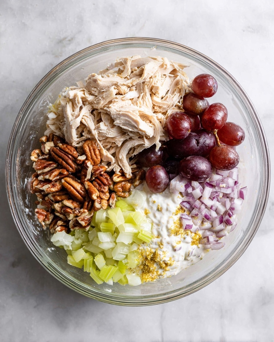 A clear glass bowl is placed on a white marbled surface, filled with six different layers arranged side by side. At the top left is a light beige shredded chicken layer with a soft texture. Next to it on the right are halved dark red grapes with a shiny, smooth surface. Below the grapes, there is a pile of finely chopped purple and white onions. Below the onions is a creamy white layer of yogurt mixed with some yellow seasoning powder. To the left of the yogurt is a cluster of brown, crunchy pecan pieces, and at the far left is a diced pale green celery layer with a slightly wet texture. Photo taken with an iphone --ar 4:5 --v 7