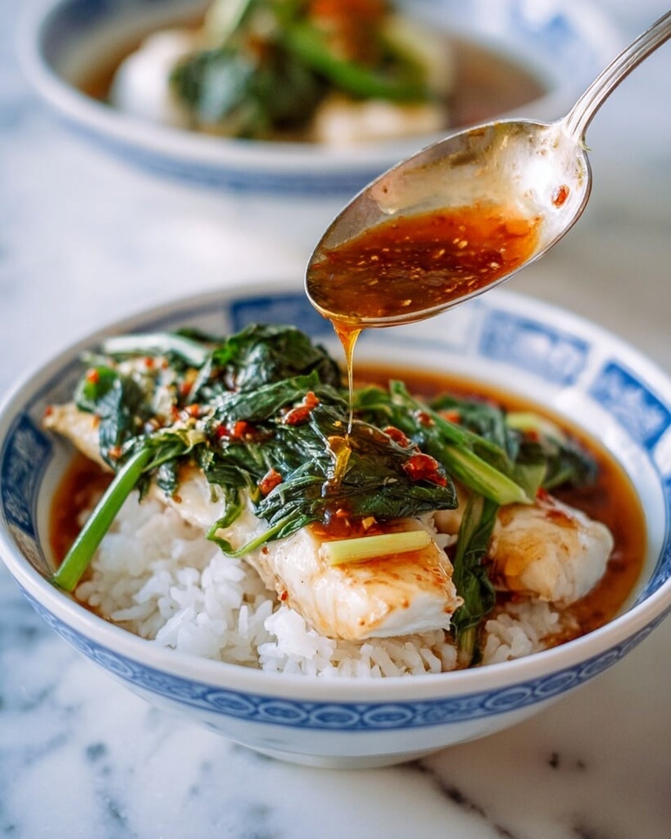The image shows a white bowl with blue patterns filled with three layers: the bottom layer is white rice with a slightly soft texture, the middle layer is a piece of light beige cooked fish, and the top layer is green leafy vegetables lightly cooked and placed on the fish. A spoon is pouring shiny, dark orange sauce over the vegetables and fish, creating a glossy look. In the blurred background, there is another white bowl with similar content visible on a white marbled surface. Photo taken with an iphone --ar 4:5 --v 7