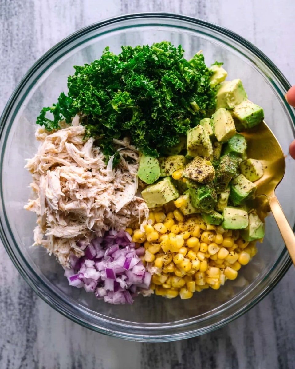 A clear glass bowl on a white marbled surface contains five neatly arranged layers of food. Starting from the top left, there is a bright green pile of chopped kale, followed to the right by light green cubes of avocado sprinkled with black pepper. Below the avocado, there is a portion of yellow corn kernels with a few black specks of seasoning. To the bottom left of the corn, there is a small mound of finely chopped purple onions. The last section on the far left consists of shredded pale beige chicken. A woman's hand holds a gold spoon above the bowl. Photo taken with an iphone --ar 4:5 --v 7