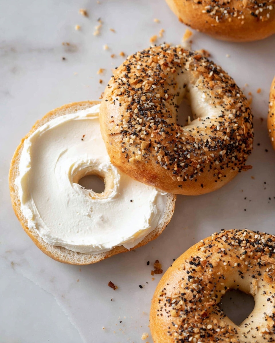 The image shows two everything bagels on a white marbled surface, one of which is open with the top half tilted to the side. The open bagel has a thick, smooth layer of white cream cheese spread evenly on its bottom half, showing the soft, light brown inside of the bagel. The top halves of both bagels are golden brown, sprinkled with a mix of black and white sesame seeds, onion flakes, and poppy seeds, giving a textured look. Another whole bagel is partially visible in the bottom right corner. Photo taken with an iphone --ar 4:5 --v 7