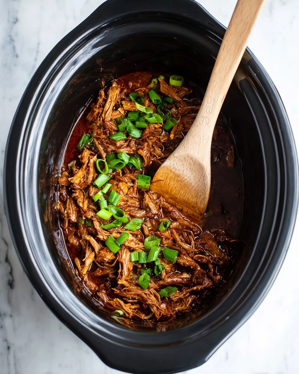 Inside a black slow cooker, there is one layer of brown shredded cooked meat mixed into a thick dark brown sauce. Bright green chopped spring onions are scattered on top of the meat, adding a fresh contrast. A light brown wooden spoon is resting inside the cooker, mixing the meat and sauce. The cooker is placed on a white marbled surface. photo taken with an iphone --ar 4:5 --v 7