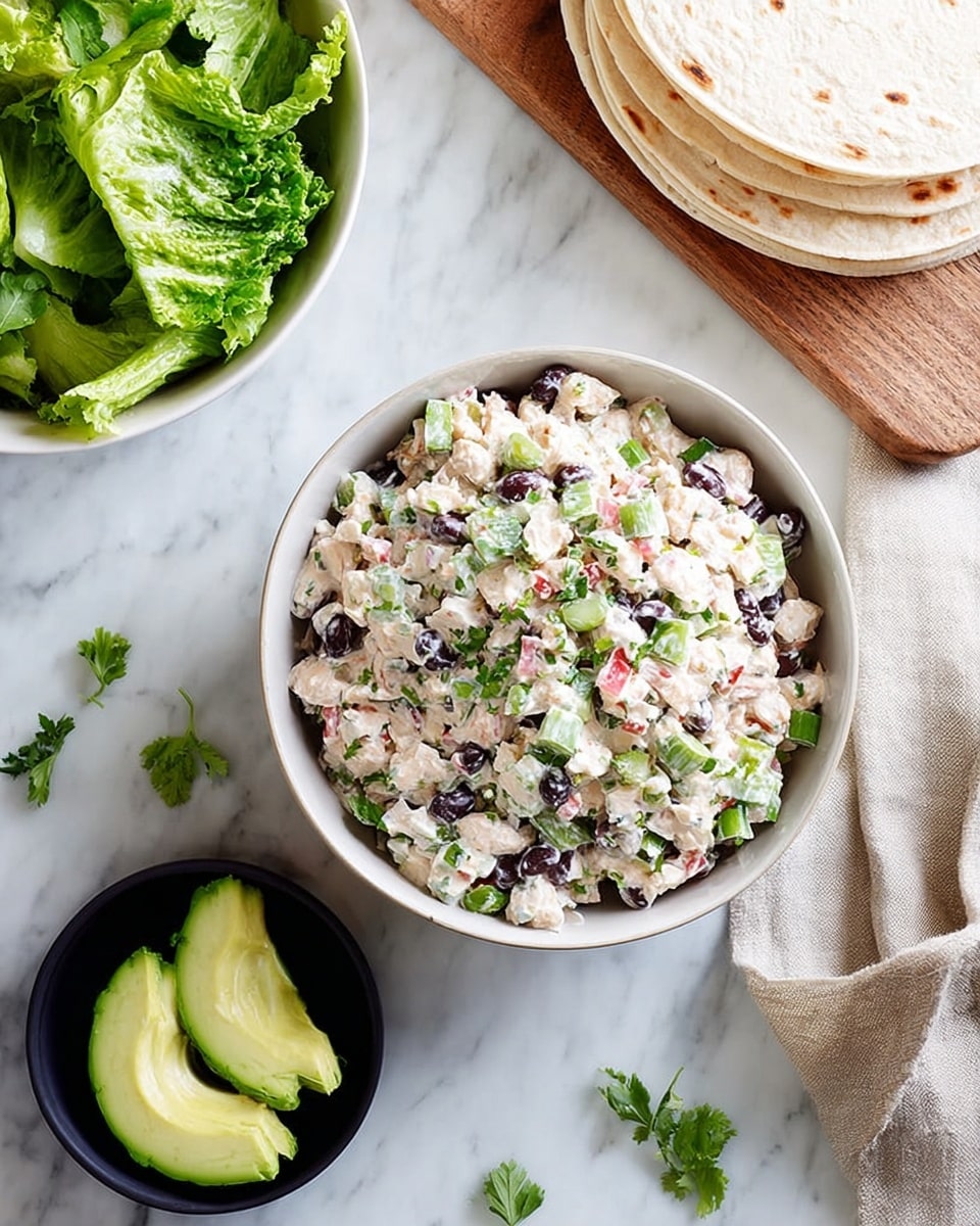 A white bowl sits on a white marbled surface filled with a creamy salad made of small beige chunks mixed with black beans, diced green onions, and bits of pink and white ingredients. The salad is topped with finely chopped green herbs. Nearby, there is a small black bowl with three slices of bright green avocado. A wooden board partially shown in the lower left holds several round, soft tortillas stacked on top of each other. In the upper left corner, a small white bowl contains fresh green leafy lettuce with a beige cloth underneath. Scattered around the bowls are a few green lettuce pieces and some leaves. photo taken with an iphone --ar 4:5 --v 7