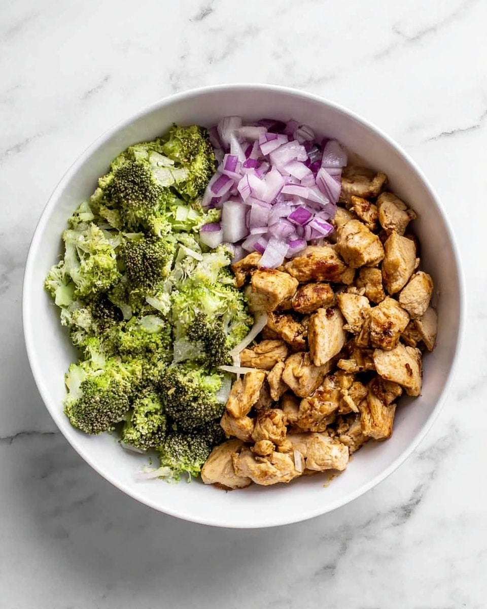 A white bowl on a white marbled surface holds three main layers of food arranged separately. On the left, there is a portion of small green broccoli florets with a rough texture. Next to the broccoli, towards the center, there is a small pile of finely chopped purple-red onions with a crisp look. On the right side, a larger section is filled with golden-brown cooked chicken pieces that have a slightly uneven texture and some browned edges. The layers are distinct and do not mix with each other. photo taken with an iphone --ar 4:5 --v 7