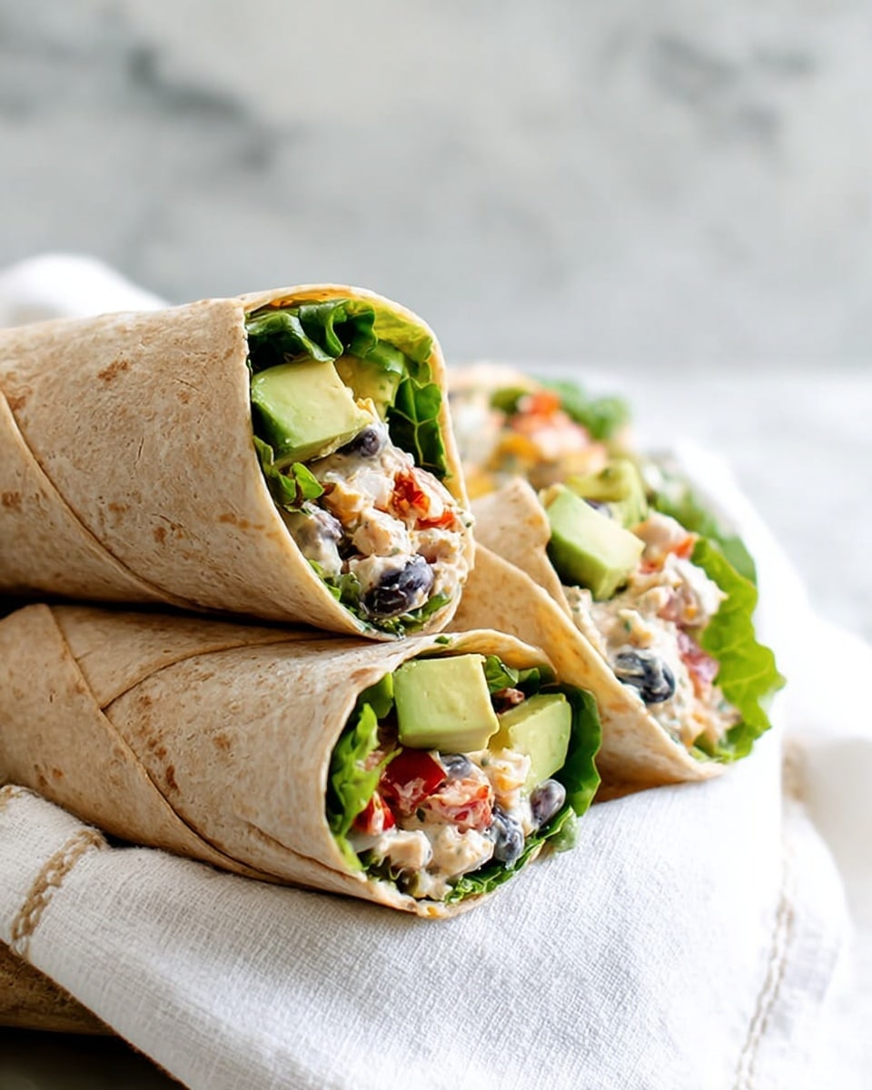 The image shows three wraps made with light brown tortillas, each wrapped loosely to hold the filling inside. The first layer inside the tortillas is leafy green lettuce visible on the outer edge. On top of the lettuce, there are chunks of bright green avocado. The main filling consists of a creamy mix with pieces of black beans, red bell peppers, and green bell peppers, creating a mix of white, black, red, and green colors in a soft texture. The wraps are placed on a white cloth with subtle lines, and the background shows a white marbled texture. Photo taken with an iphone --ar 4:5 --v 7