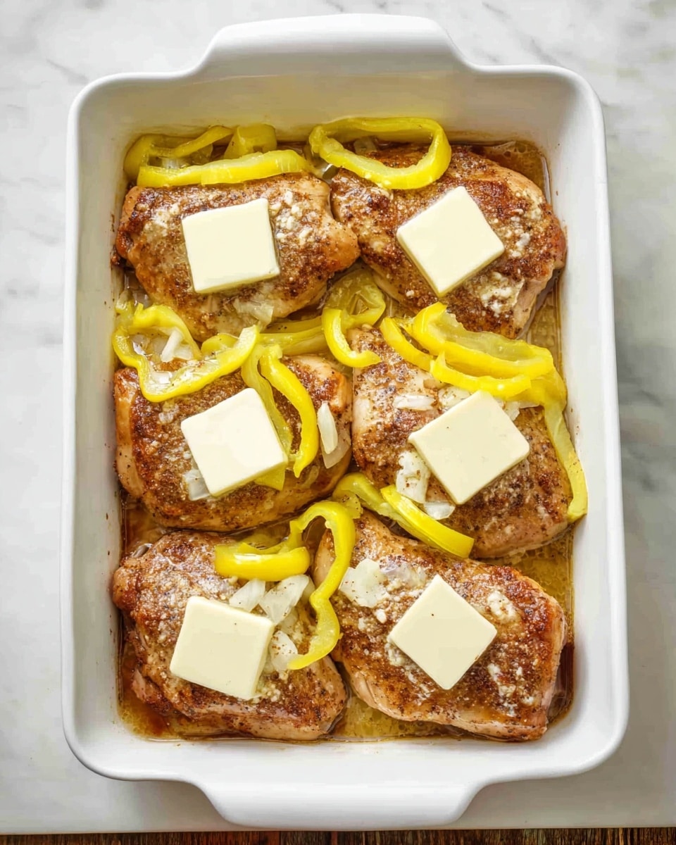 The image shows a white rectangular baking dish filled with four large browned chicken pieces arranged in two rows, about two pieces per row. Each piece is topped with several thin, spiral-shaped yellow pepper slices. On top of the chicken and peppers, there are evenly spaced squares of butter, melting slightly. The dish rests on a white marbled surface, creating a clean and bright background. The texture of the chicken looks juicy with a light coating of seasoning visible beneath the butter and peppers. photo taken with an iphone --ar 4:5 --v 7