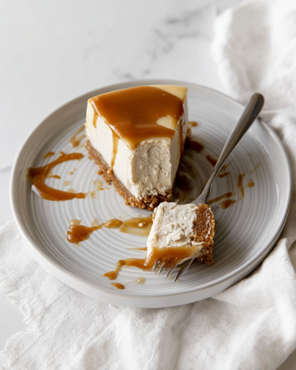A white round plate with light grey rings holds a cheesecake slice divided into two pieces. The bottom layer is a brown crumbly crust, the middle layer is thick and creamy white cheese, and the top layer is smooth caramel sauce dripping slightly on one piece. A silver fork resting on the plate has creamy cheese and caramel smears around it, with more caramel sauce streaked across the plate. The plate is on a white marbled surface with a soft white cloth partially visible underneath. Photo taken with an iphone --ar 4:5 --v 7