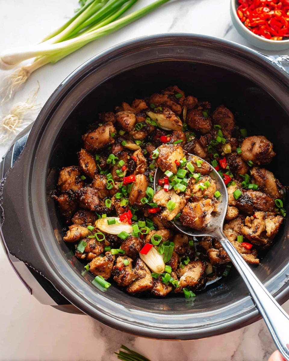 The image shows a black pot filled with small pieces of cooked meat that are dark brown with some charred edges, mixed with sliced light golden garlic and small red chili pieces. Bright green chopped scallions are sprinkled on top, adding fresh color. A metal spoon is scooping some of the meat from the pot. The pot is placed on a white marbled surface with a few whole scallions around it and a small bowl with red chopped ingredients blurred in the background. photo taken with an iphone --ar 4:5 --v 7