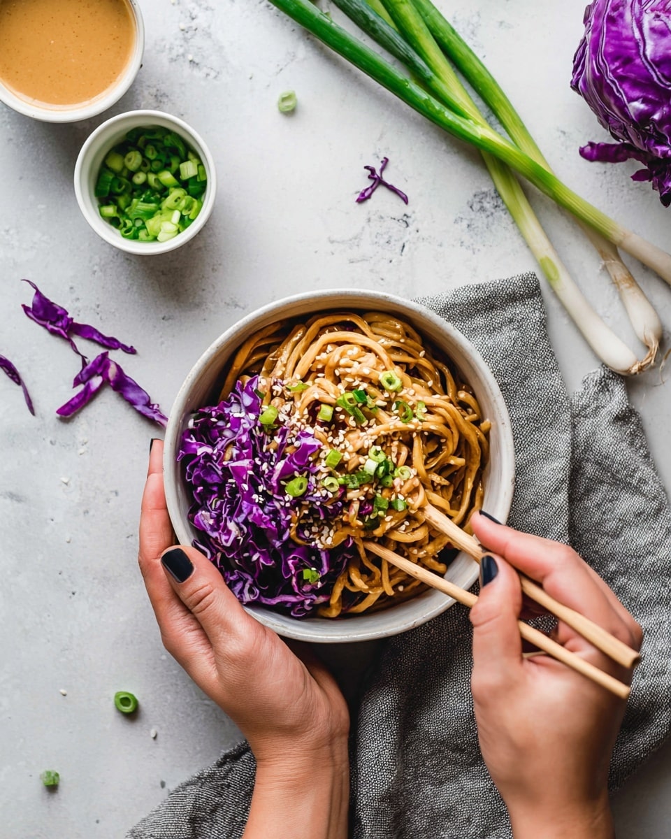 A white bowl filled with a noodle dish showing three visible layers: light brown noodles on top with a slightly glossy texture, bright green chopped scallions mixed in, and vibrant purple shredded cabbage on one side. Scattered white sesame seeds sit on the noodles, adding small dots of color. A woman's hand with dark nail polish holds the bowl from one side, while another woman's hand uses light wooden chopsticks to lift some purple cabbage. Surrounding the bowl are two smaller white bowls, one with more chopped scallions and the other with a smooth light brown sauce. Three whole green scallions lie on a textured gray cloth on a white marbled surface, which also holds scattered pieces of purple cabbage. Photo taken with an iphone --ar 4:5 --v 7