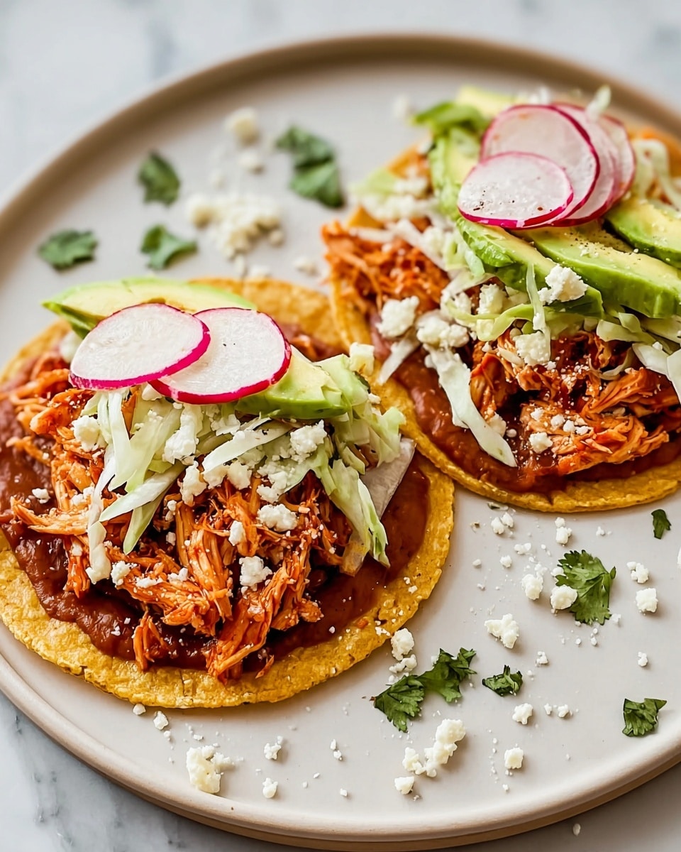 Two small yellow corn tortillas lie flat on a white plate over a white marbled surface. Each tortilla has a base layer of brown refried beans spread across it. On top of the beans, there is a layer of thinly sliced white cabbage on the right side, and few slices of round radish with white centers and red edges arranged in a fan shape. Next, with slices of green avocado laid diagonally, shredded orange-red seasoned chicken is piled on top. Finally, the chicken is sprinkled with small white crumbles of cheese and bits of chopped green cilantro. Some extra cheese crumbles and cilantro pieces are scattered on the plate. Photo taken with an iphone --ar 4:5 --v 7