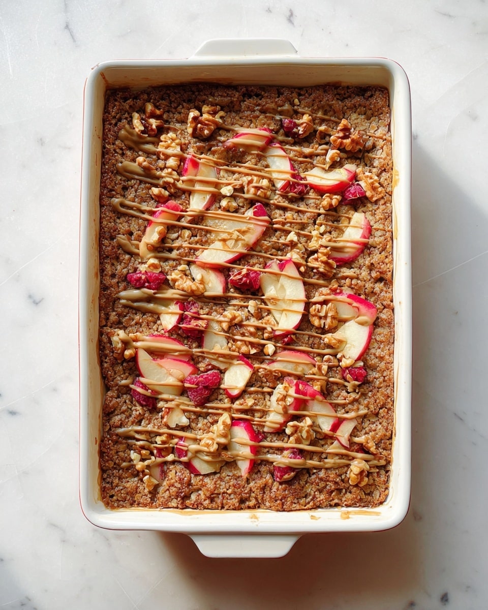A wooden bowl holds one square piece of oat and walnut bar topped with thin, light red apple slices. The bar looks crumbly with visible oats and walnut pieces spread throughout. A silver fork inside the bowl has a small bite-sized piece of the bar on it. In the background, there is a yellow baking dish with more oat bars inside. A few walnut halves and apple pieces are scattered on a white marbled surface around the bowl, and a white cloth with grey stripes is partly visible on the side. photo taken with an iphone --ar 4:5 --v 7
