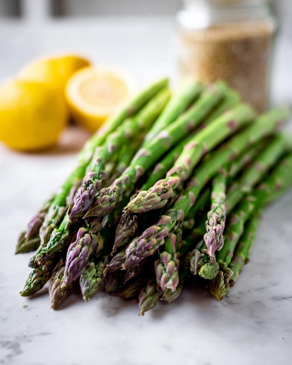 A close-up of a bundle of fresh green asparagus spears laid side by side horizontally on a white marbled surface. The tips of the asparagus show detailed small buds with a mix of purple and green hues, while the lower ends fade to a lighter green. In the background, there is a jar with a blurred light brown content and two bright yellow lemon halves, all sitting on the same white marbled surface. The lighting is soft and natural, highlighting the fresh texture of the asparagus. Photo taken with an iphone --ar 4:5 --v 7