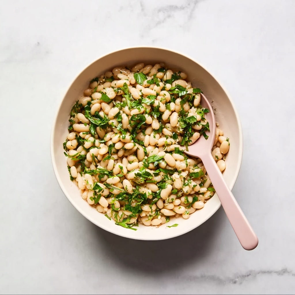 A round white bowl filled with a pearl couscous salad mixed with chopped fresh green herbs evenly spread throughout. A light pink spoon rests inside the bowl on the right side, partially buried in the couscous. The bowl sits on a white marbled surface with subtle gray veins. The overall colors are soft beige from the couscous and bright green from the herbs, with the pink spoon adding a gentle touch of color. photo taken with an iphone --ar 4:5 --v 7