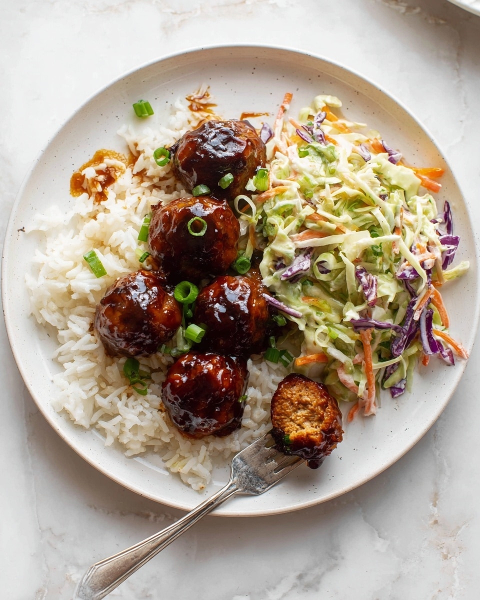 A white round plate is arranged with three main parts: first, there is a layer of cooked white rice at the bottom left, slightly sticky with some brown sauce spots. On top of the rice, there are five small, round shaped meatballs glazed in a glossy dark brown sauce, garnished with chopped green onions. To the right side of the meatballs is a colorful coleslaw made from thin strips of green cabbage, orange carrots, and purple cabbage, mixed with a creamy dressing and small pieces of green herbs. A silver fork with a meatball is placed on the bottom right edge of the plate. The plate sits on a white marbled surface. Photo taken with an iphone --ar 4:5 --v 7