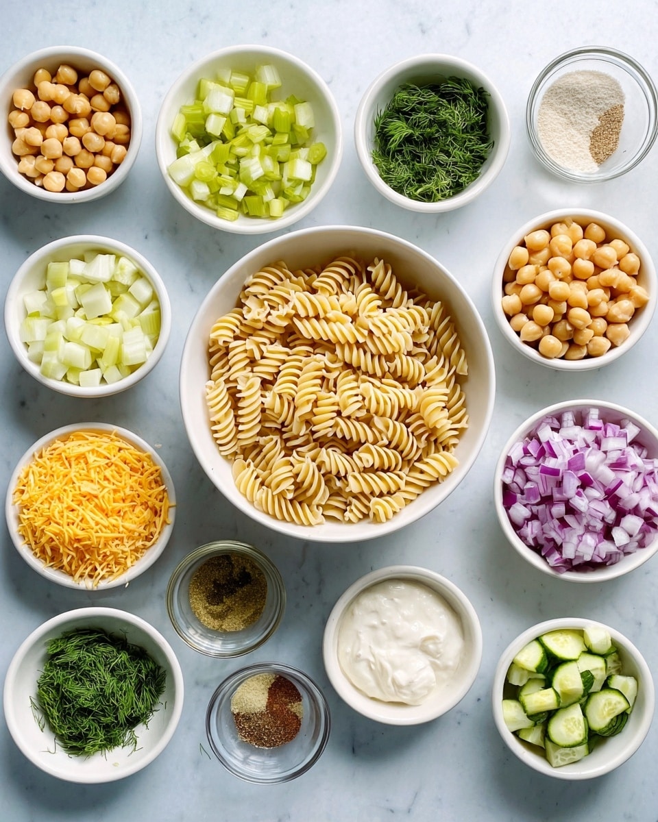 A top-down view shows several small white bowls arranged neatly on a white marbled surface. In the center is a bowl filled with uncooked spiral pasta, light beige in color. Around it are smaller bowls containing different ingredients: chickpeas with a pale yellow color, cubed pickles with green and yellow tones, diced celery in light green, chopped red onions in purple, chopped cucumbers with green skin and pale flesh, bright orange shredded cheese, fresh chopped parsley and dill herbs, and small amounts of various powders and liquids including a creamy white mayo-like sauce, white yogurt, a pale yellow oil, and seasoning powders in shades of light brown, black, and white. Each bowl's texture varies from smooth to chunky. The clean, organized layout creates a fresh, bright cooking preparation scene photo taken with an iphone --ar 4:5 --v 7