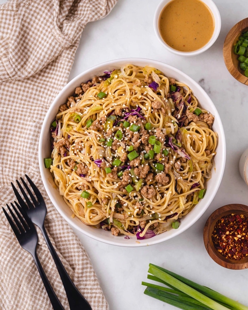 The image shows a white bowl filled with a noodle dish that has three main layers. The bottom layer is light brown cooked noodles mixed with small pieces of cooked ground meat. The middle layer includes thin slices of cooked cabbage and bits of purple cabbage scattered throughout. The top layer is sprinkled with chopped green onions and white sesame seeds for a fresh, colorful touch. The bowl is placed on a white marbled surface, next to two black forks on a beige checkered cloth, a small wooden bowl of red chili flakes, a small white bowl of light brown sauce, and some green onion stalks. Photo taken with an iphone --ar 4:5 --v 7