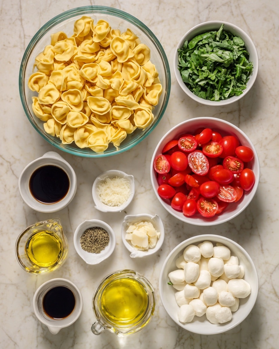 In the image, there is a large clear glass bowl at the top left filled with yellow tortellini pasta. To the right, two small white bowls hold chopped green leafy herbs in different sizes. Below the pasta, a white bowl contains halved red cherry tomatoes, showing their juicy interiors. Surrounding these, smaller white bowls hold various ingredients: one with minced garlic, one with salt and black pepper, one with dried herbs, and one with small white mozzarella balls. Two clear glass pitchers, one with light yellow oil and the other with dark balsamic vinegar, are placed near the bottom left. All items sit on a white marbled surface. Photo taken with an iphone --ar 4:5 --v 7