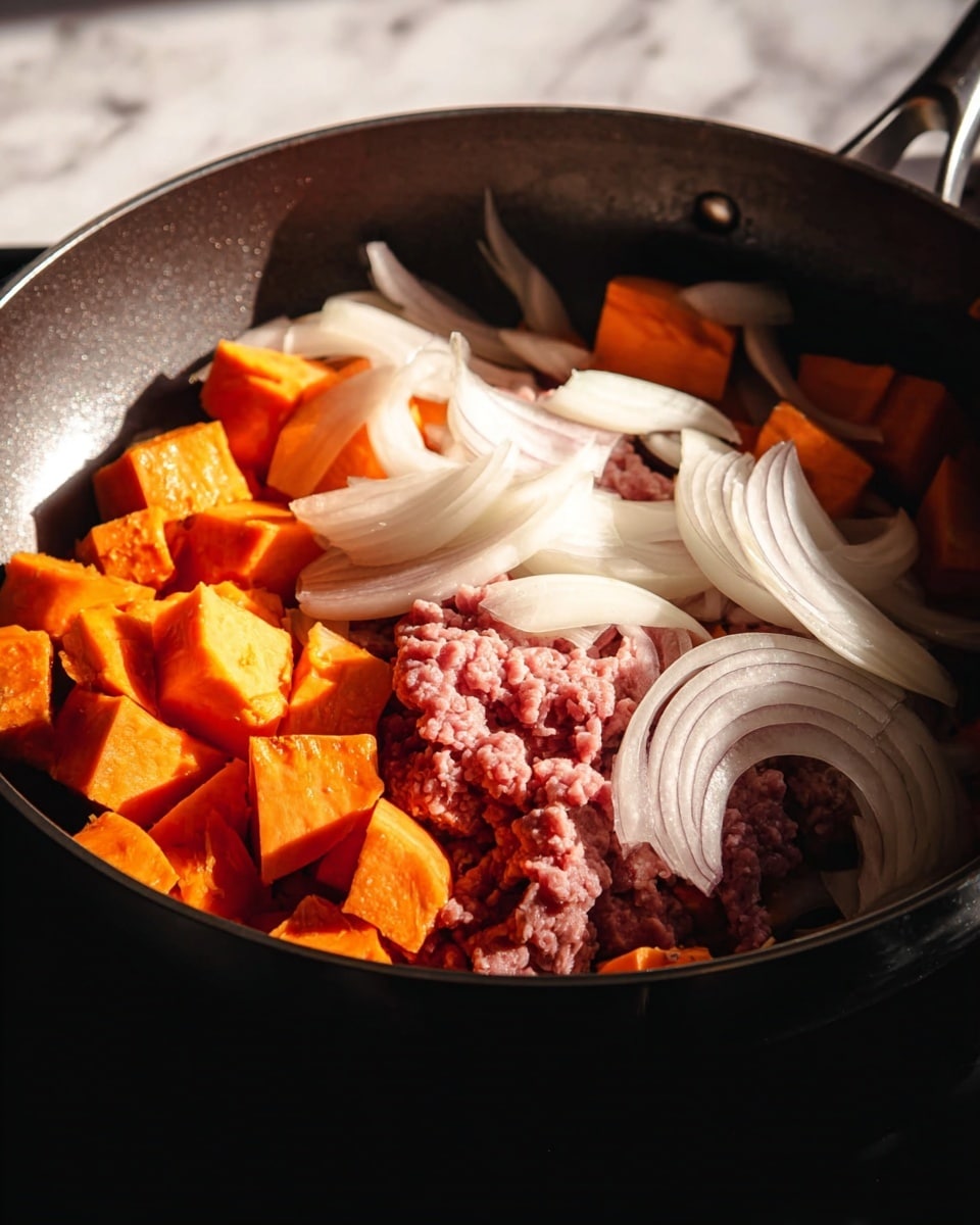 In a dark frying pan, there are three main layers: at the bottom, bright orange cubes of sweet potato with bits of skin showing; on one side, raw pink ground meat piled in a small mound; and on top and around the meat and sweet potatoes, thin white slices of onion arranged loosely. The lighting casts warm sunlight highlighting the colors and textures clearly, with the pan’s edges visible but dark. The background is a white marbled texture. photo taken with an iphone --ar 4:5 --v 7