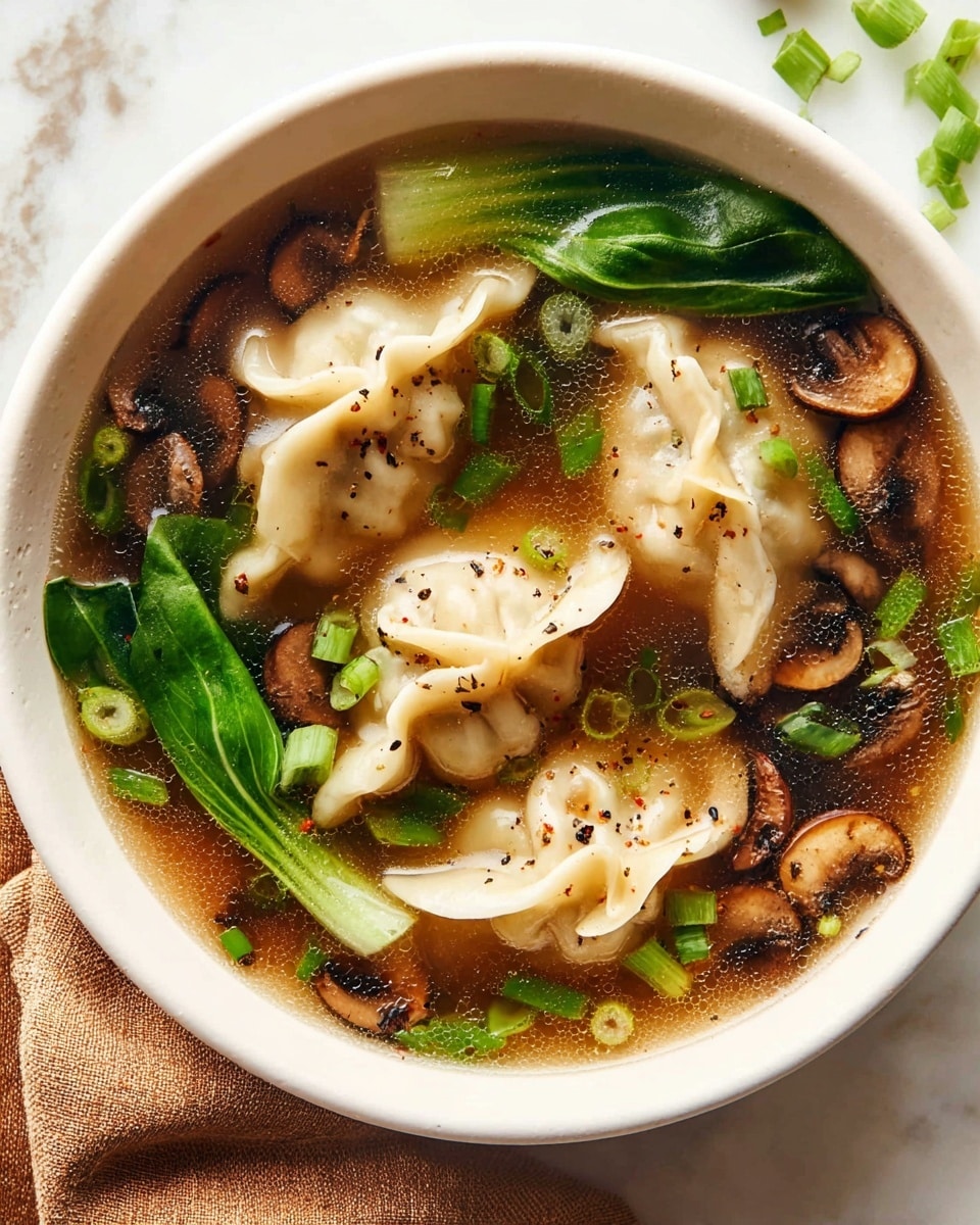 A white bowl filled with clear brown broth, showing three soft, light beige dumplings floating near the center. The dumplings have crinkled edges and are sprinkled with small black pepper specks. Bright green chopped scallions are scattered on top and within the soup, along with several dark brown sliced mushrooms and several long green leafy vegetables resting near the bowl edges. The bowl sits on a white marbled surface with a soft brown cloth partially visible in the lower left corner. photo taken with an iphone --ar 4:5 --v 7