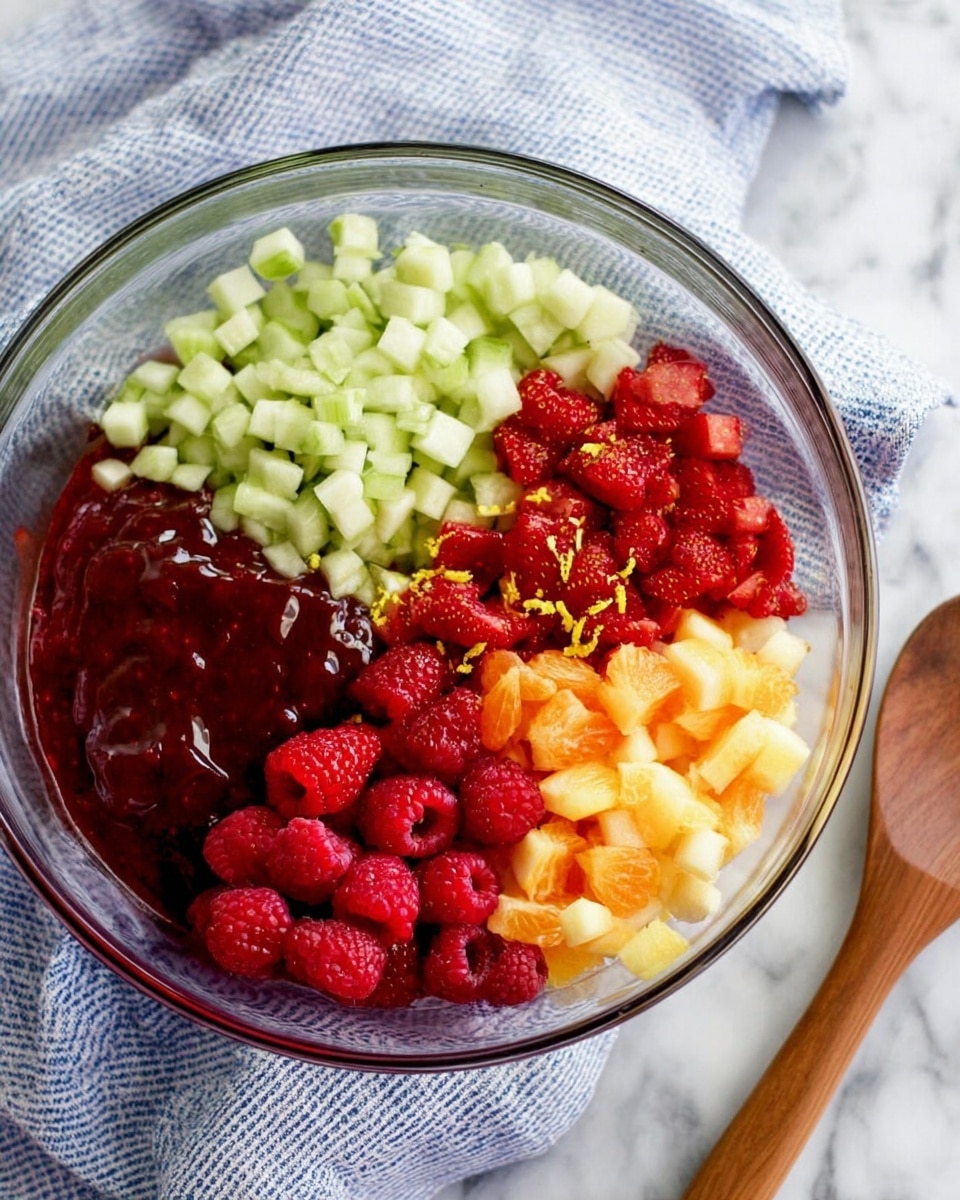 A clear glass bowl sits on a white marbled surface with a blue and white cloth beneath it and a wooden spoon nearby. Inside the bowl, there are five distinct layers arranged around each other. At the top right is a layer of small, pale green cubed pieces with a crisp texture. On the bottom right, there are bright red chopped strawberries mixed with a little yellow zest. At the bottom, a layer of small, soft orange cubes. On the bottom left, a cluster of fresh red raspberries with a slightly bumpy surface. In the center is a glossy dark red thick sauce or jam, shiny and smooth. photo taken with an iphone --ar 4:5 --v 7