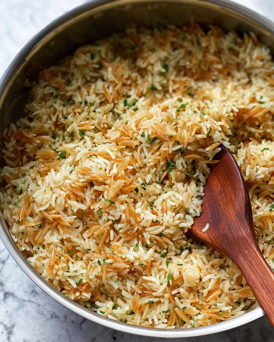 A close-up of cooked rice mixed with small toasted pasta pieces, showing a mix of light yellow and golden brown colors with green herbs sprinkled throughout. The rice and pasta mix fills a silver pot, and a wooden spoon scoops some of the mixture. The background is a white marbled texture. Photo taken with an iphone --ar 4:5 --v 7