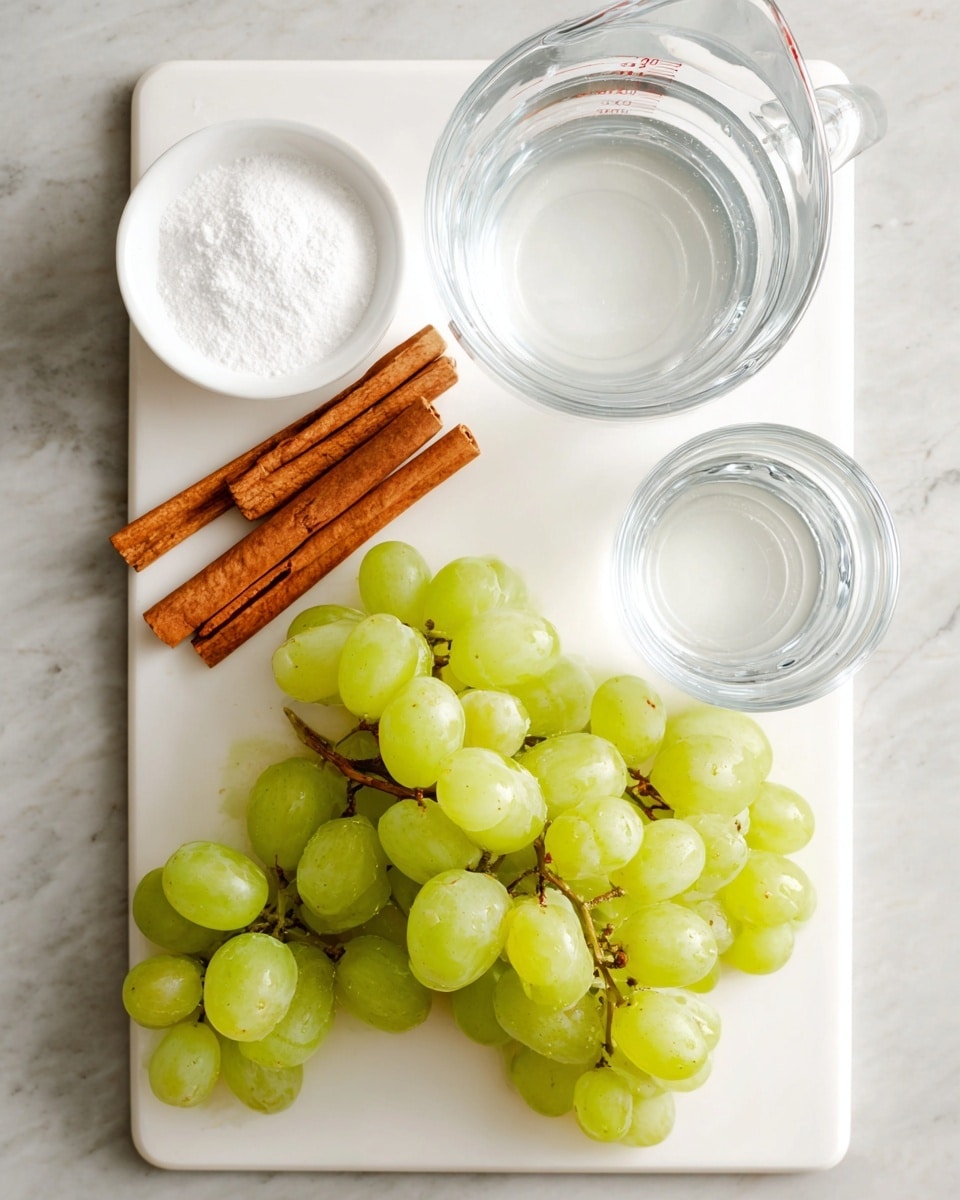 The image shows a white cutting board with a bunch of light green grapes placed on the bottom right side. On the top left side, there are two cinnamon sticks placed diagonally next to a small white bowl filled with a white powder, likely sugar. In the top center and right are two clear glass measuring cups, one filled with water and the other filled with a white liquid. The cutting board is set on a white marbled surface with soft natural light. Photo taken with an iphone --ar 4:5 --v 7