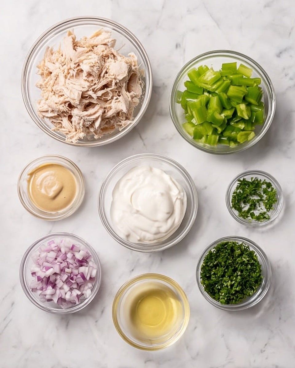 The image shows seven clear glass bowls with different ingredients placed on a white marbled surface. The largest bowl, located on the top left, contains light brown shredded chicken. To its right, there is a medium bowl filled with small green chopped celery pieces. Next to this is another medium bowl holding smooth white sour cream. Below these, a small bowl with beige mustard is placed on the left. In the center, there is a small bowl with pale yellow lemon juice. To the right bottom corner, a small bowl contains finely chopped green herbs. The last small bowl, located in the bottom middle, displays finely chopped red onion. The bowls are neatly arranged and all sit on a white marbled background. photo taken with an iphone --ar 4:5 --v 7
