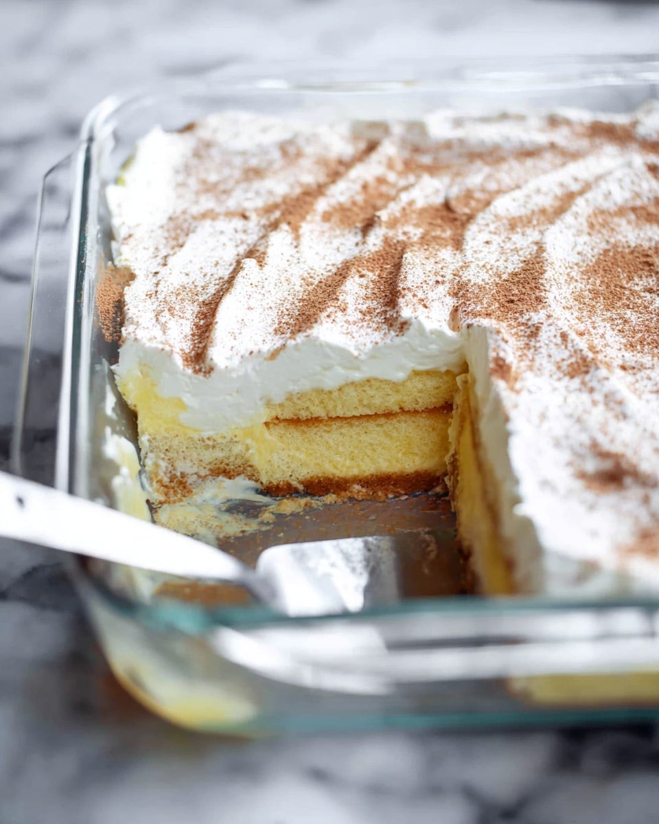 The image shows a clear glass rectangular baking dish with a layered dessert inside. The dessert has three visible layers: a bottom layer of light yellow sponge cake soaked in cream, a middle layer of white creamy custard, and a top layer of thick white whipped cream dusted evenly with light brown cinnamon powder. A portion is missing from the corner, revealing the layers more clearly, and a metal spatula with a white handle rests inside the dish near the missing piece. The background is a white marbled surface, adding a clean and bright look. Photo taken with an iphone --ar 4:5 --v 7