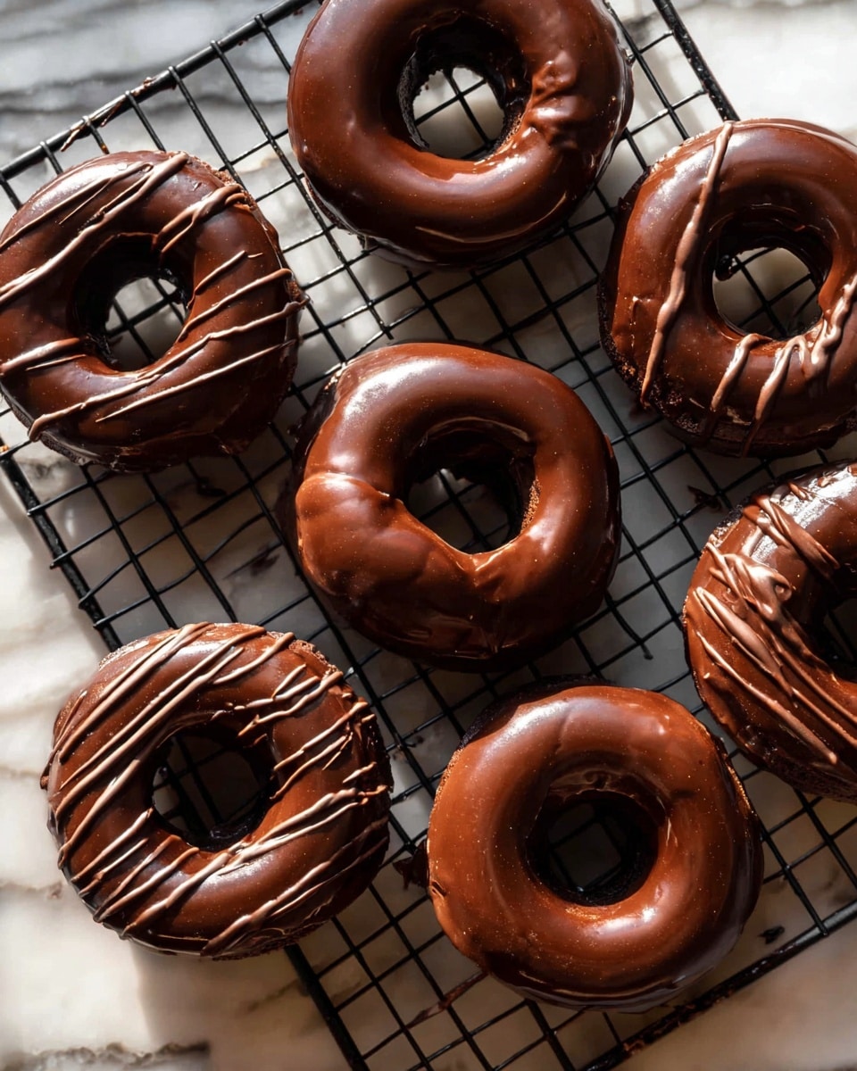 The image shows six round donuts with a smooth, dark brown chocolate coating all over, some topped with thin, lighter brown chocolate drizzle lines. The donuts are arranged on a black wire cooling rack over a white marbled surface. The chocolate glaze on the donuts looks shiny and thick, covering the pastry fully. Light shines softly on the donuts, creating a warm and rich look. Photo taken with an iphone --ar 4:5 --v 7