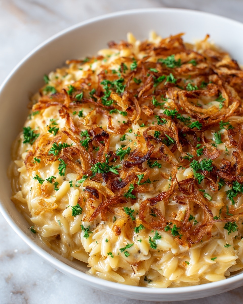 A close-up of a white bowl filled with creamy orzo pasta mixed with melted cheese, topped with crispy golden brown fried onions scattered evenly over the surface, and sprinkled with small pieces of fresh green parsley all around. The orzo has a soft and smooth texture with a light yellow color, and the fried onions add a crunchy contrast with a darker golden shade. The bowl sits on a white marbled surface with a soft light highlighting the rich textures of the dish. Photo taken with an iphone --ar 4:5 --v 7