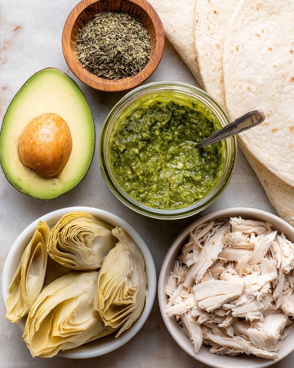 The image shows a top view of several food items on a white marbled surface. There is a halved avocado with a smooth green and yellow texture and a large seed in the center. Next to it is a glass jar filled with bright green pesto sauce with a thick, slightly chunky texture, and a silver spoon inside. A small wooden bowl holds a mix of dried green herbs. At the bottom left, a white bowl contains pale yellow artichoke hearts with layered, soft leaves. On the bottom right, another white bowl is filled with shredded cooked chicken that is light beige with fibrous texture. There are also white soft tortillas folded at the top right corner. Photo taken with an iphone --ar 4:5 --v 7