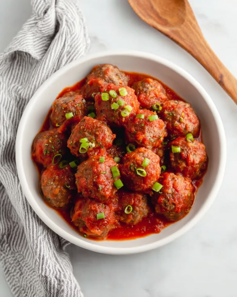 A white bowl filled with about fifteen meatballs covered in a red tomato sauce, each meatball topped with small chopped green onions. The bowl is placed on a white marbled surface with a soft striped cloth nearby and a wooden spoon resting to the side. photo taken with an iphone --ar 4:5 --v 7