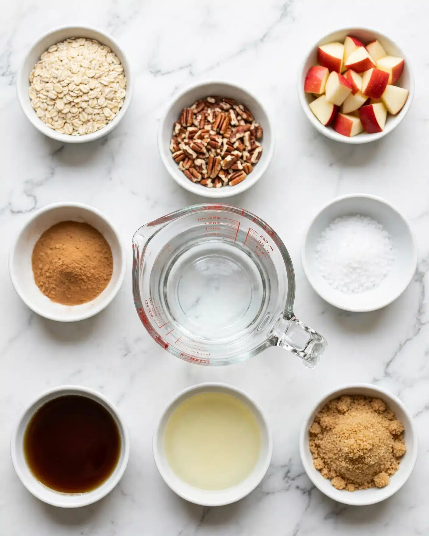 Apple Cinnamon Oatmeal Recipe 4 The image shows eight small white bowls and a clear glass measuring cup with water arranged on a white marbled surface. The bowls each contain one ingredient: one bowl is full of pale beige oats, another has chopped red and white apple pieces, a third bowl holds chopped pecans with brown and light nut colors, a fourth bowl has a light brown cinnamon powder, a fifth bowl contains dark amber maple syrup, a sixth bowl has clear vanilla liquid, and a seventh bowl is filled with white sea salt. The glass measuring cup is filled with clear water. Each bowl and the cup are spaced evenly in a neat, flat lay composition. photo taken with an iphone --ar 4:5 --v 7